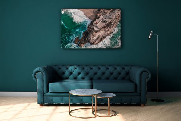 Aerial coastal print above teal sofa in modern living room, Nazare, Portugal.