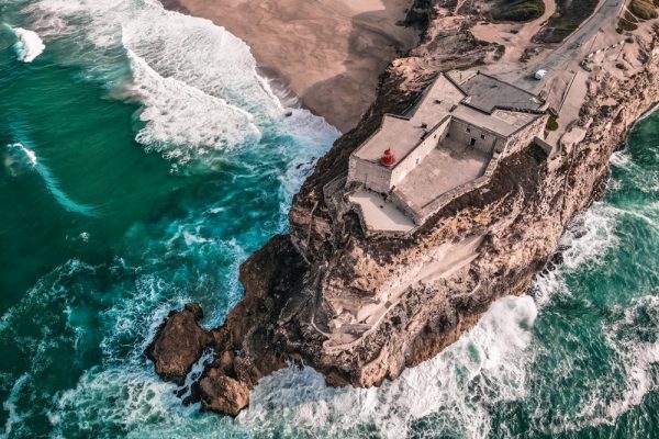 Aerial view of Nazare lighthouse and cliffs above the ocean waves.
