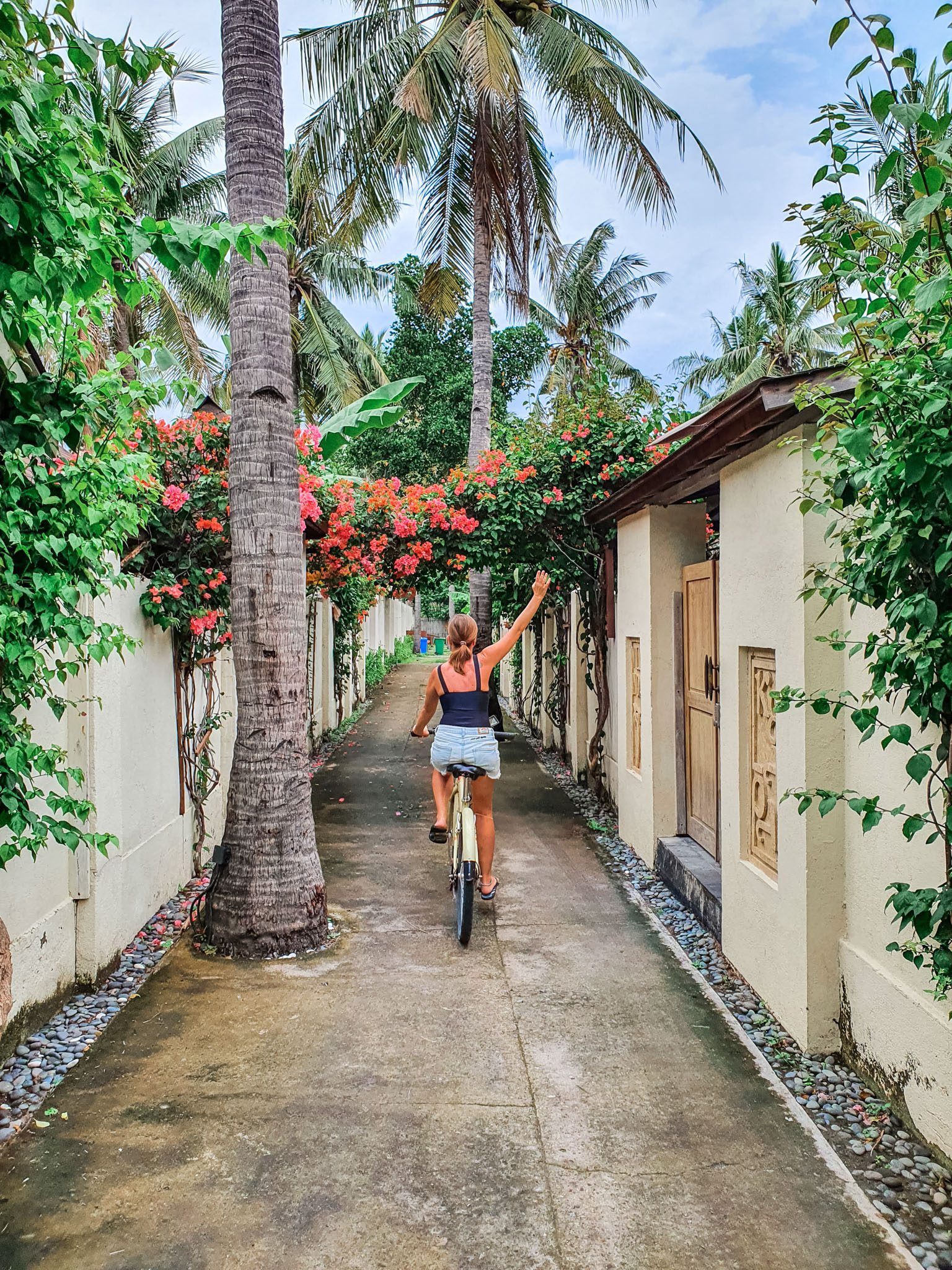 A woman cycling through a palm-lined pathway in the Gili Islands.