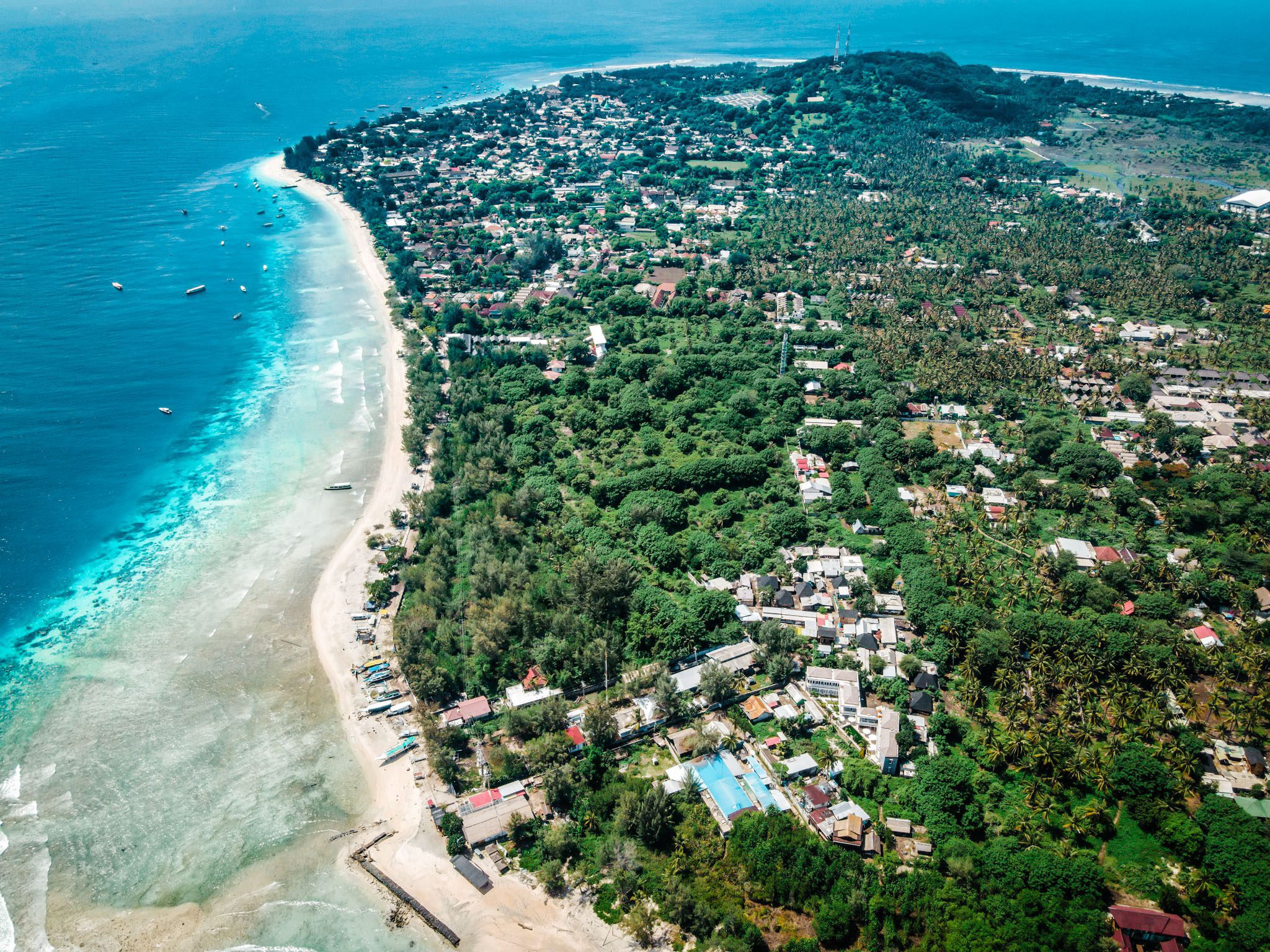 Aerial view of lush landscapes and coastline of Gili Islands, featuring vibrant waters and buildings.