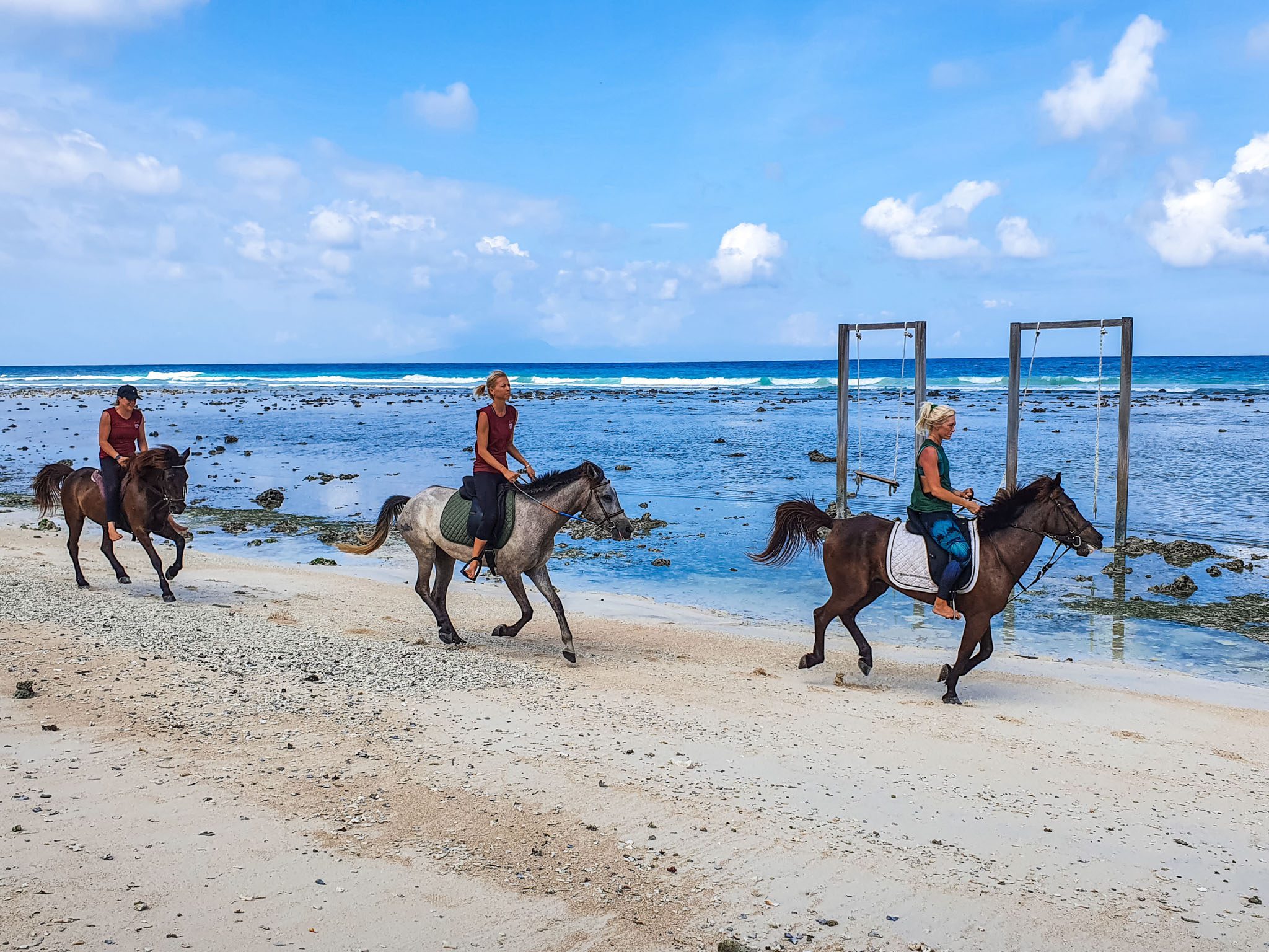 People horseback riding along a sandy beach on the Gili Islands with a clear ocean view.
