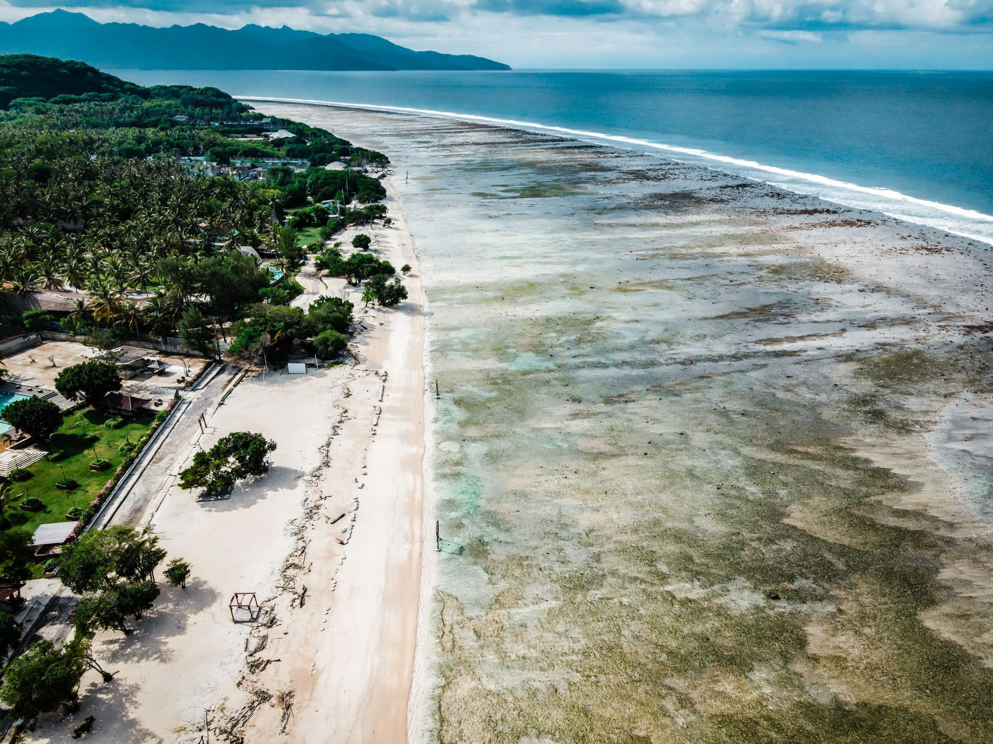 Aerial view of sandy beach and lush greenery along the coast of Gili Islands.