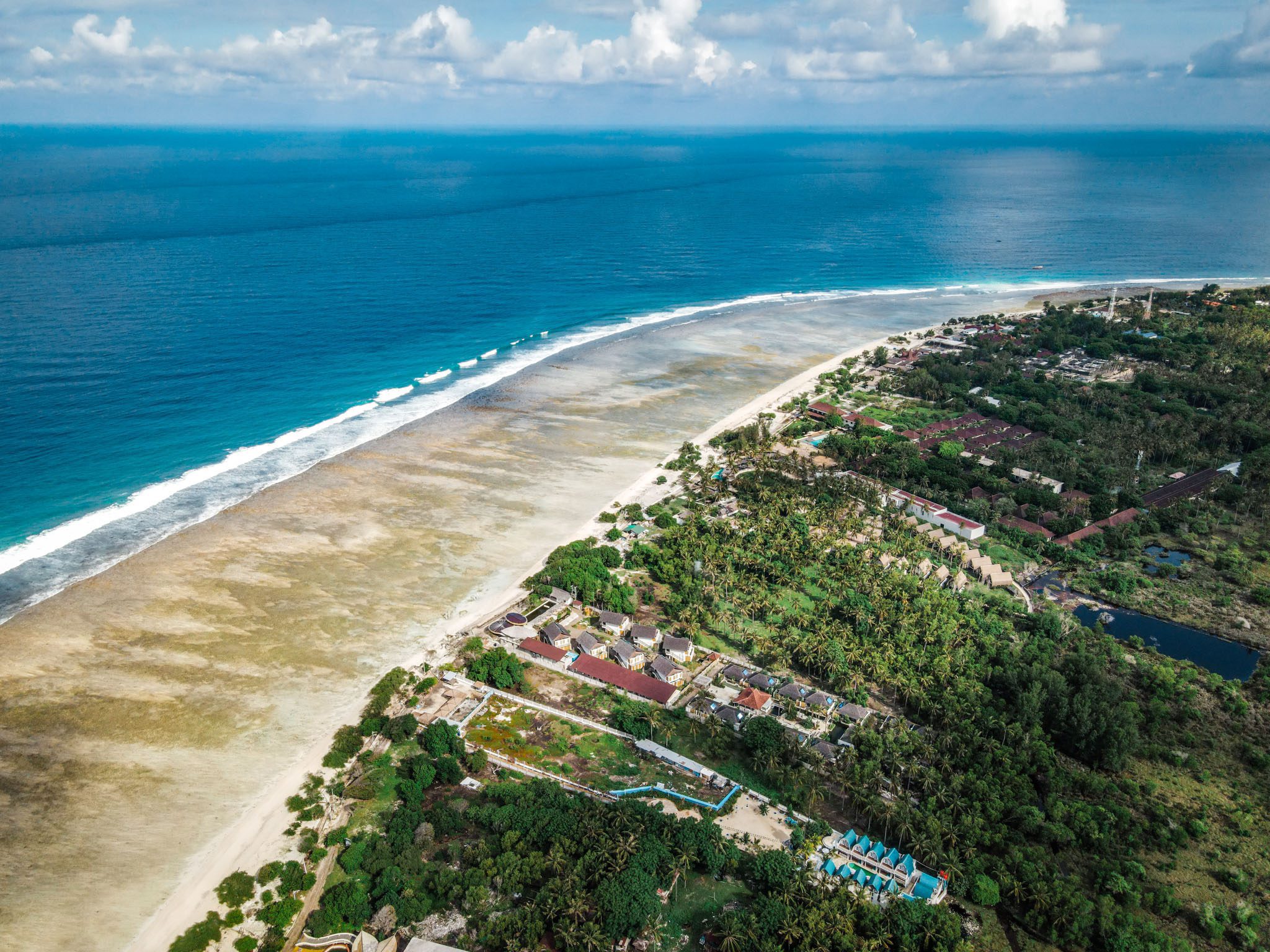 Aerial view of turquoise ocean and lush greenery on Gili Islands coastline.