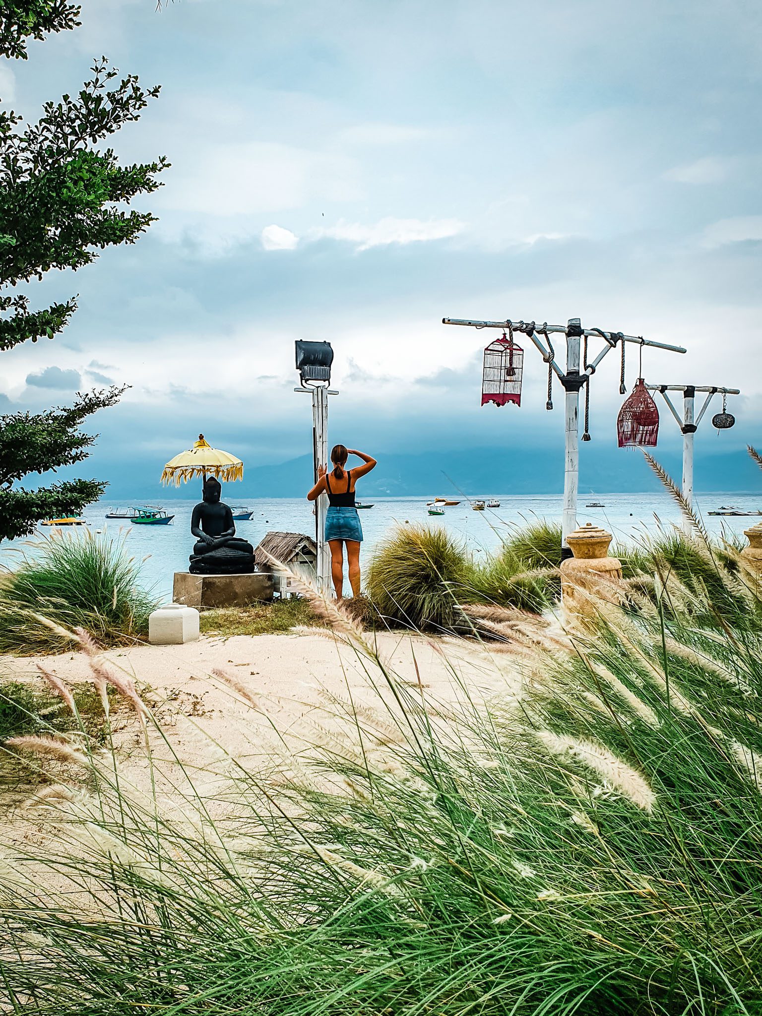 Beach view with a woman and Buddha statue overlooking the sea in Gili Islands.