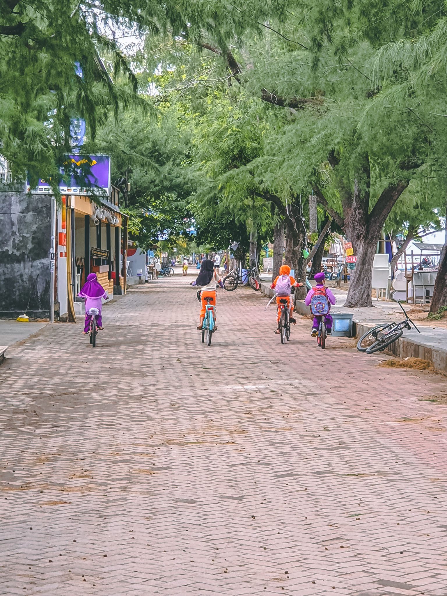 Children cycling along a tree-lined path in the Gili Islands.