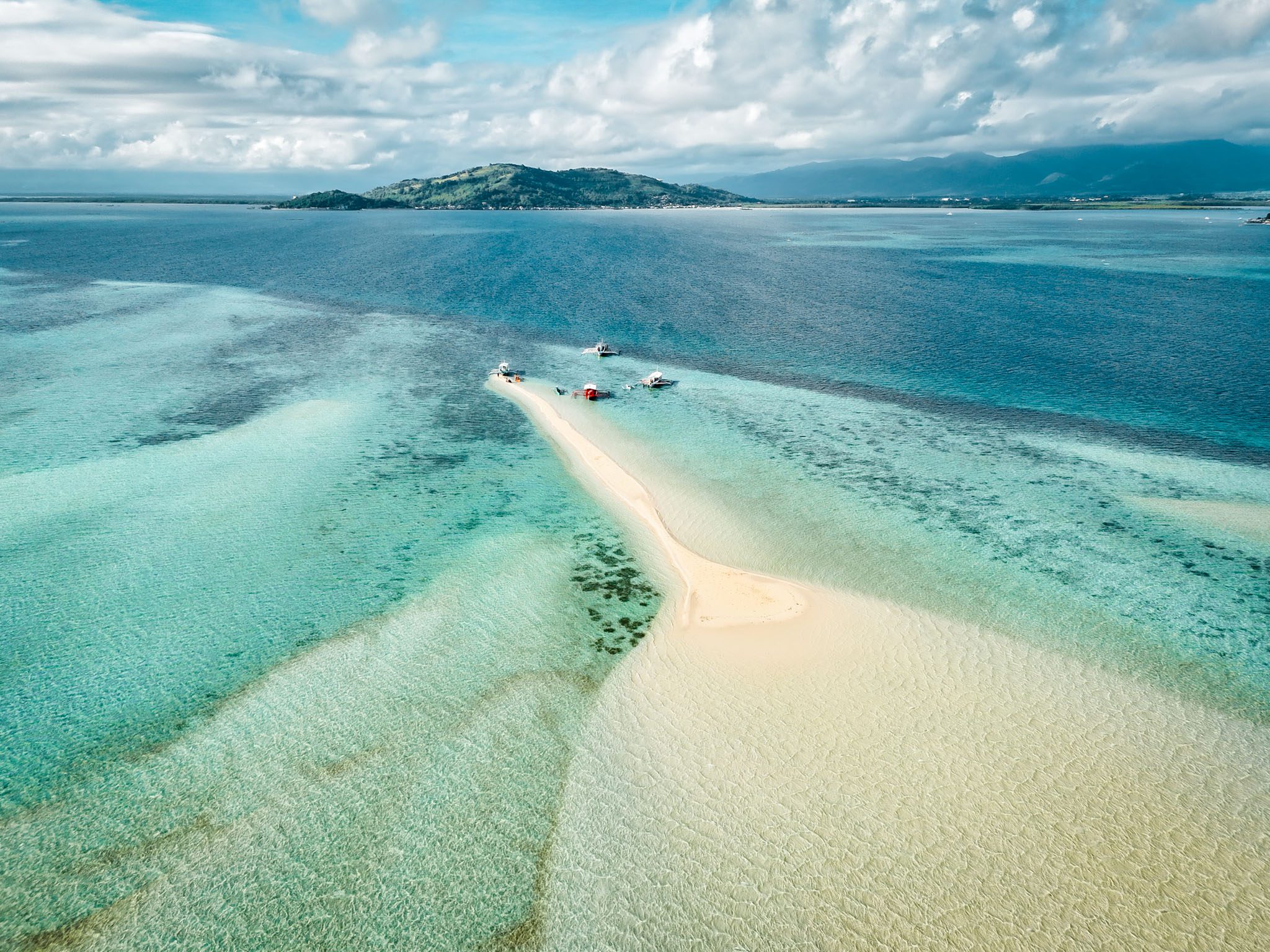 Aerial view of a sandbar in turquoise waters near Dumaguete, Philippines, with boats docked.