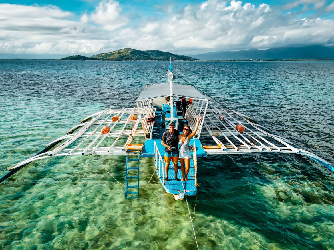 Couple on a traditional boat in Dumaguete, Philippines, surrounded by clear turquoise waters.