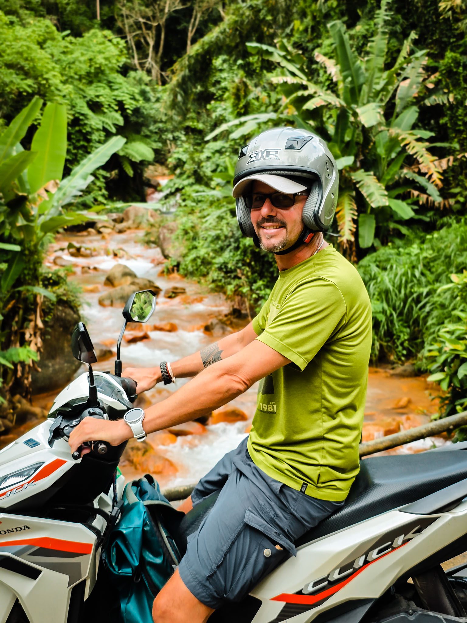 Man on motorcycle beside lush stream in Dumaguete, Philippines jungle setting.