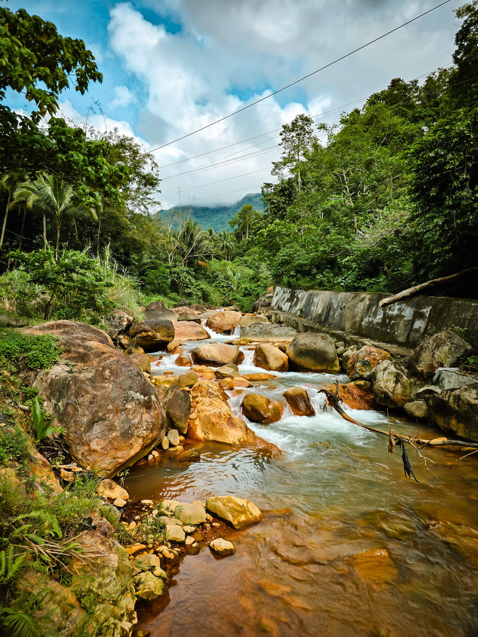 Rocky stream in lush greenery near Dumaguete, Philippines under a cloudy sky.