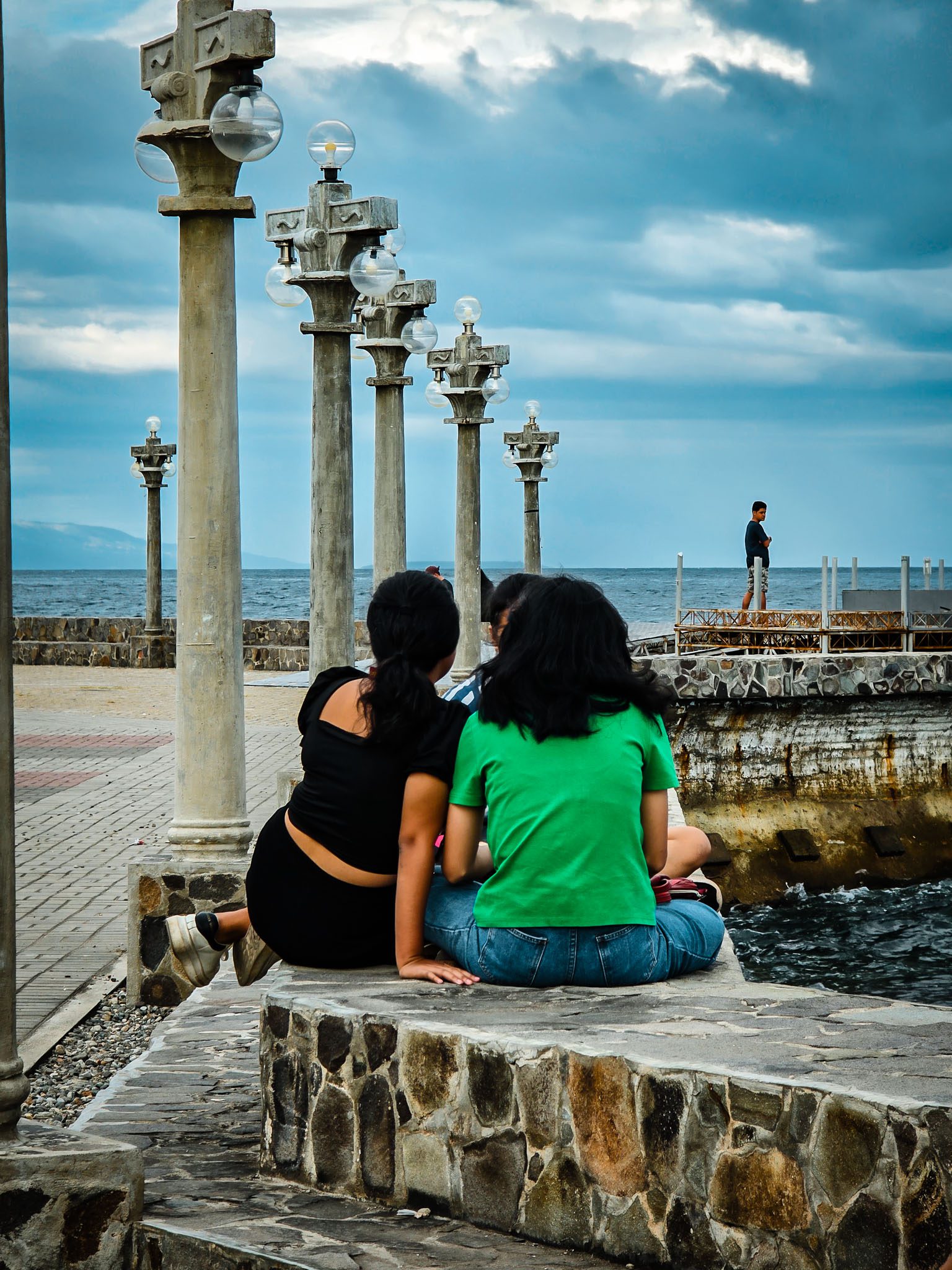 Group of friends sitting by the sea with cloudy sky in Dumaguete, Philippines.