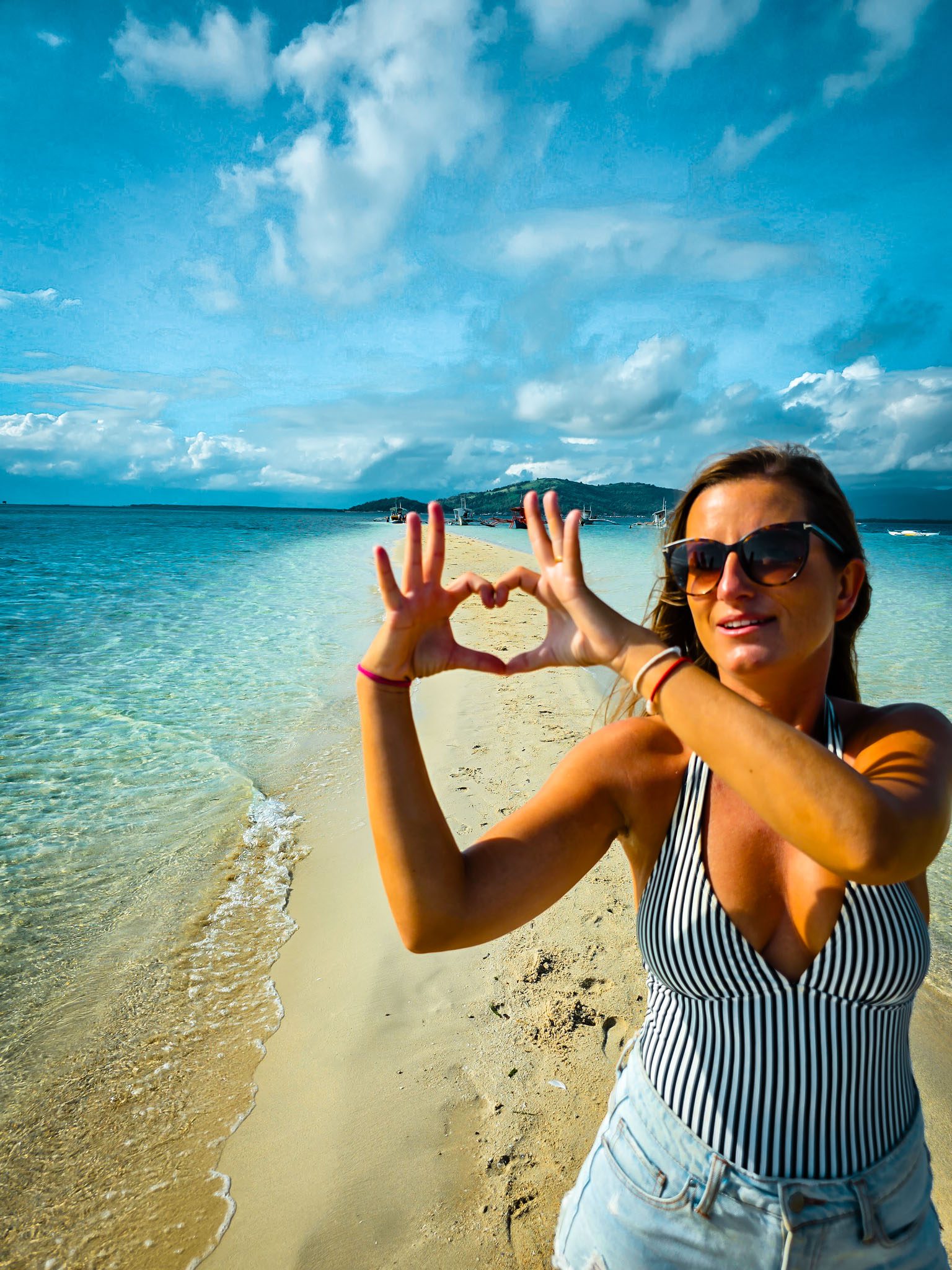 Woman forming heart shape by the beach in Dumaguete, Philippines with clear blue waters.