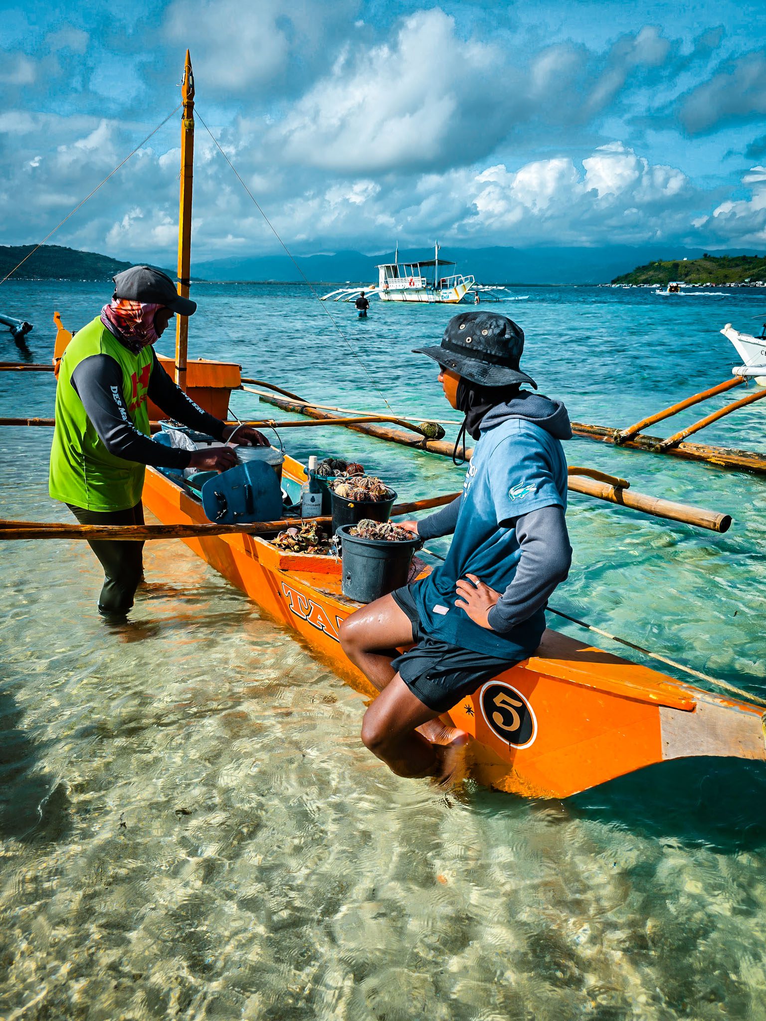 Fishermen in Dumaguete, Philippines prepare for work on an orange boat in clear blue waters.