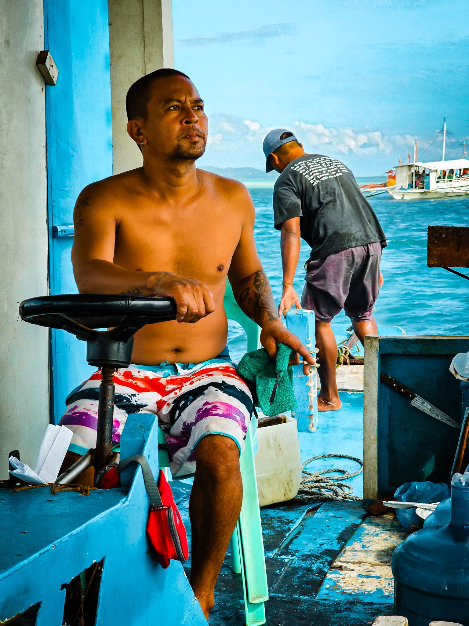 Two fishermen on a boat in Dumaguete, Philippines, with vivid blue sea and sky.