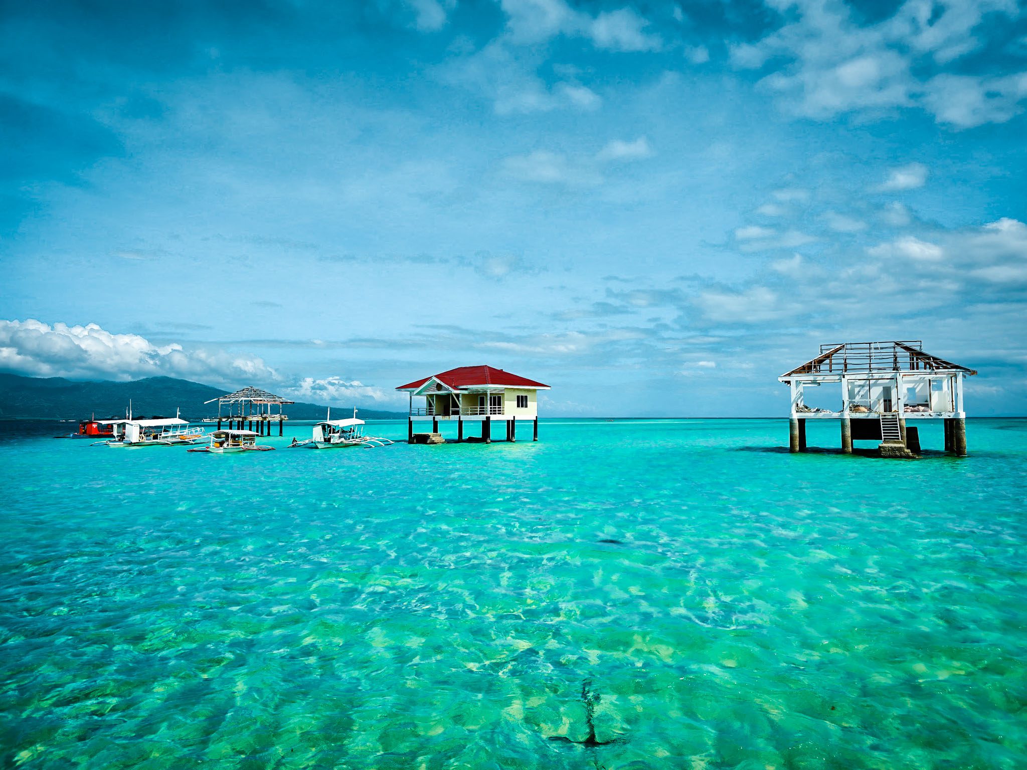 Stilt houses over turquoise waters in Dumaguete, Philippines, under a clear blue sky.