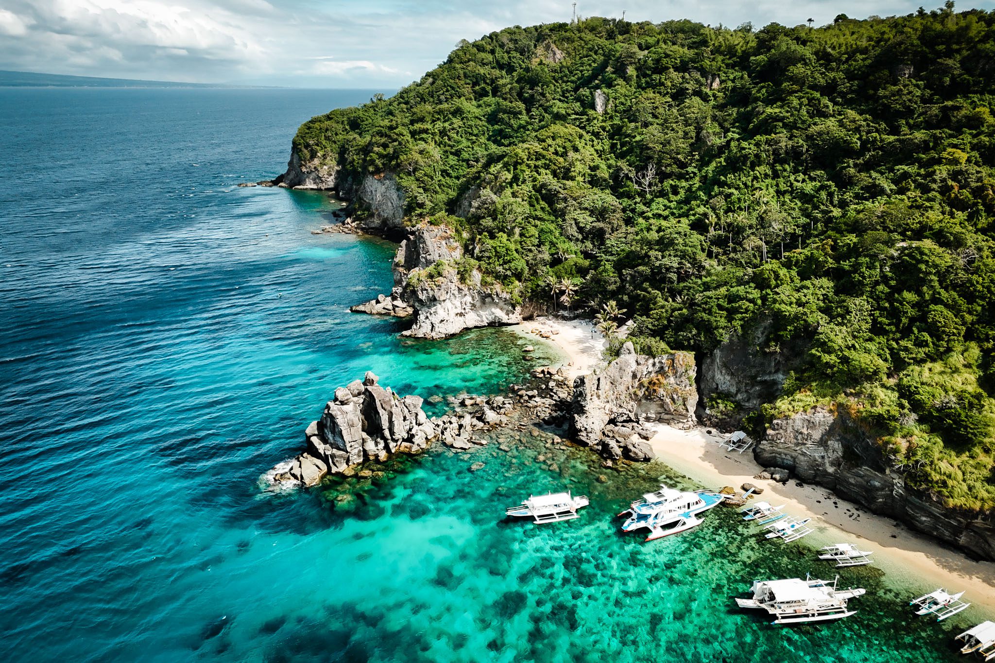 Aerial view of a lush coastline with boats and clear blue waters in Dumaguete, Philippines.