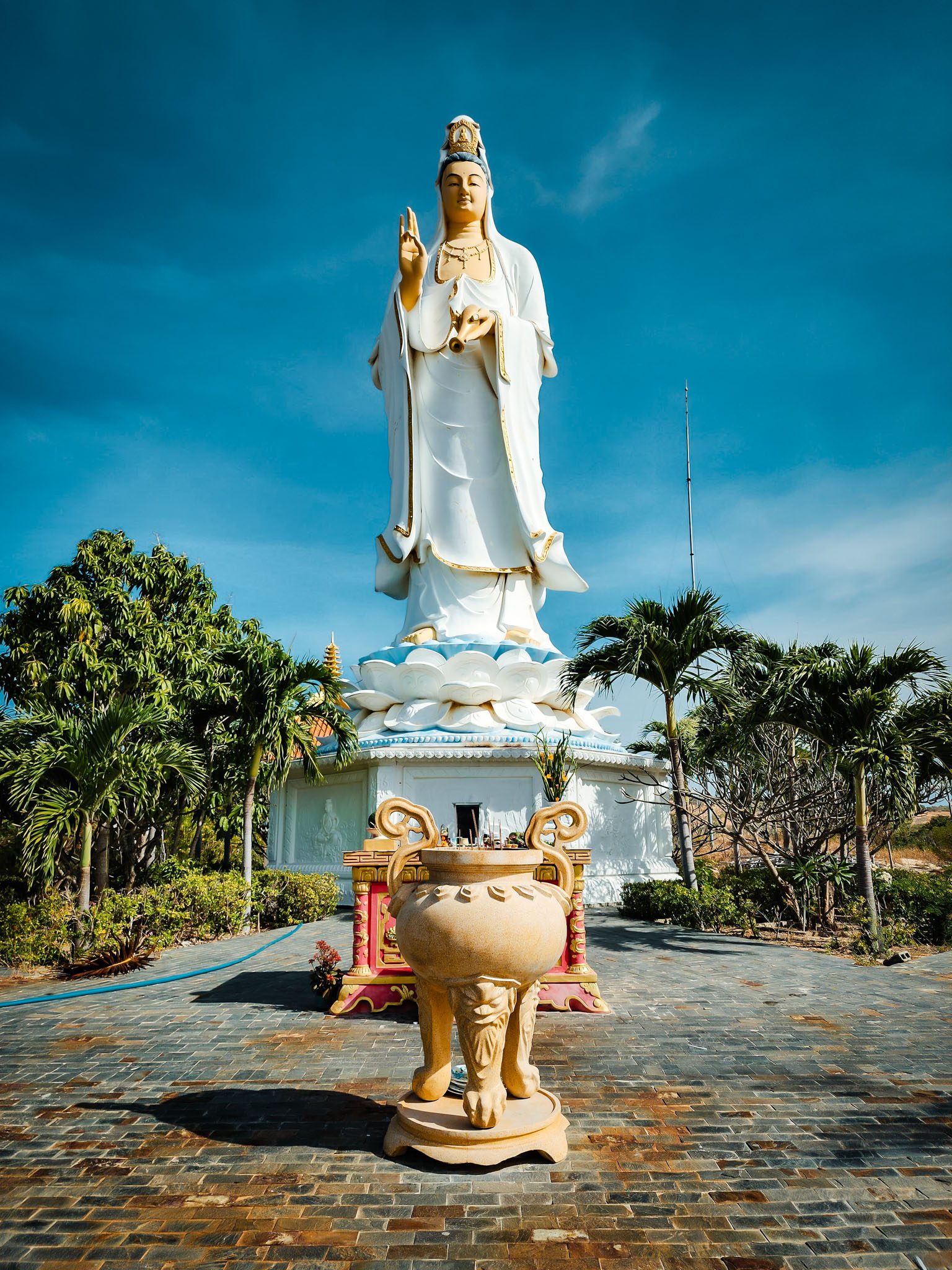 Tall Buddha statue in a serene garden setting in Mui Ne, Vietnam under a clear blue sky.