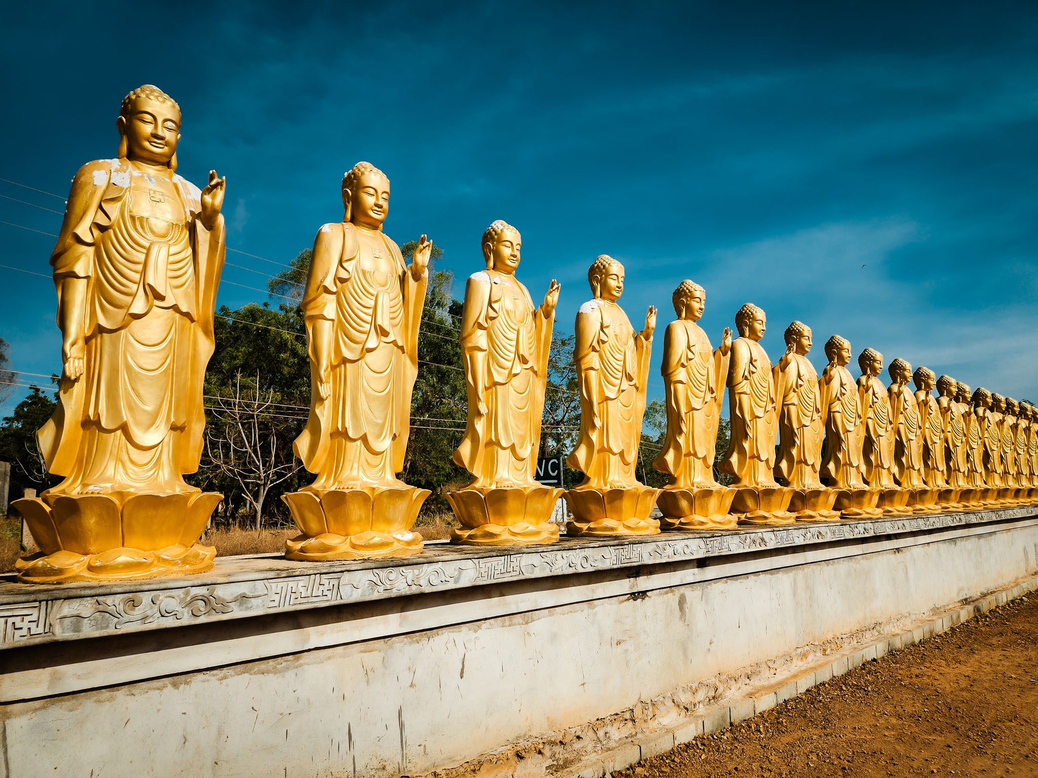Golden Buddha statues in a row under a clear sky in Mui Ne, Vietnam.