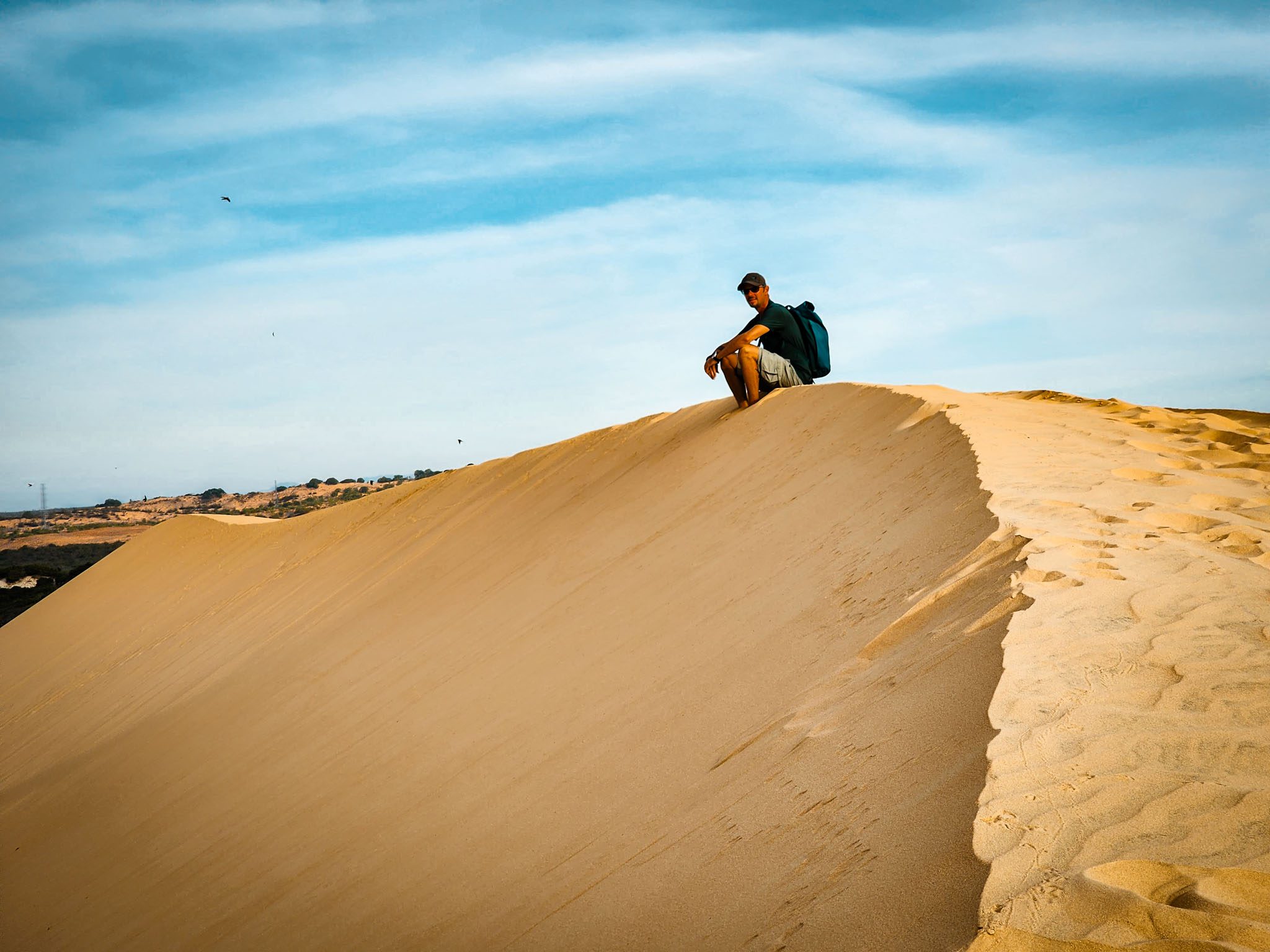 Person sitting on sand dune in Mui Ne, Vietnam under blue sky.
