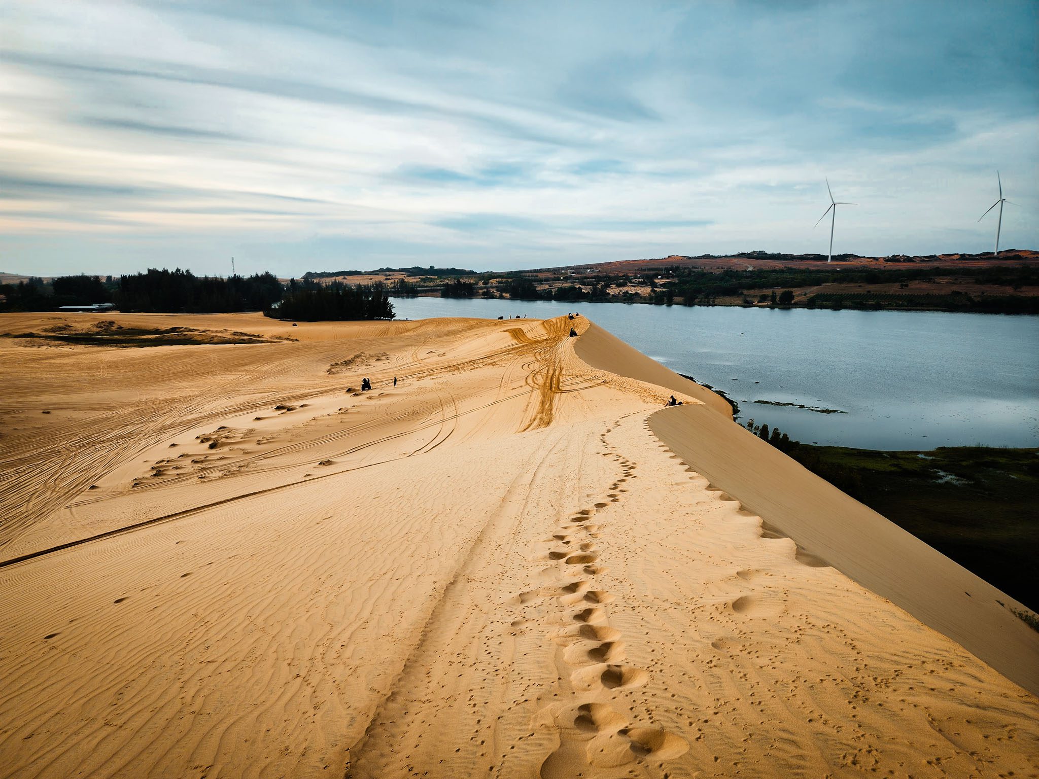 Golden sand dunes near a lake in Mui Ne, Vietnam, with wind turbines in the distance.