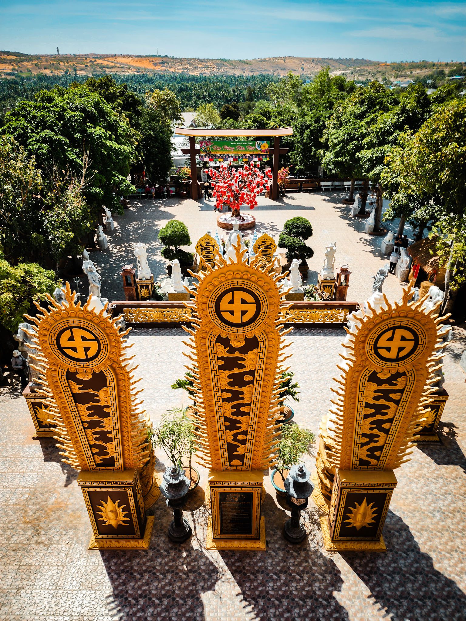 Golden temple gate and garden in Mui Ne, Vietnam, surrounded by lush greenery and statues.