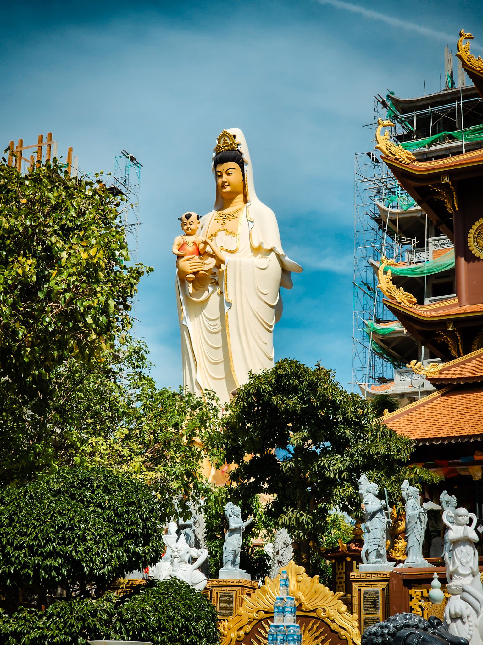 Statue of Guanyin holding a child at a temple in Mui Ne, Vietnam, surrounded by lush greenery.