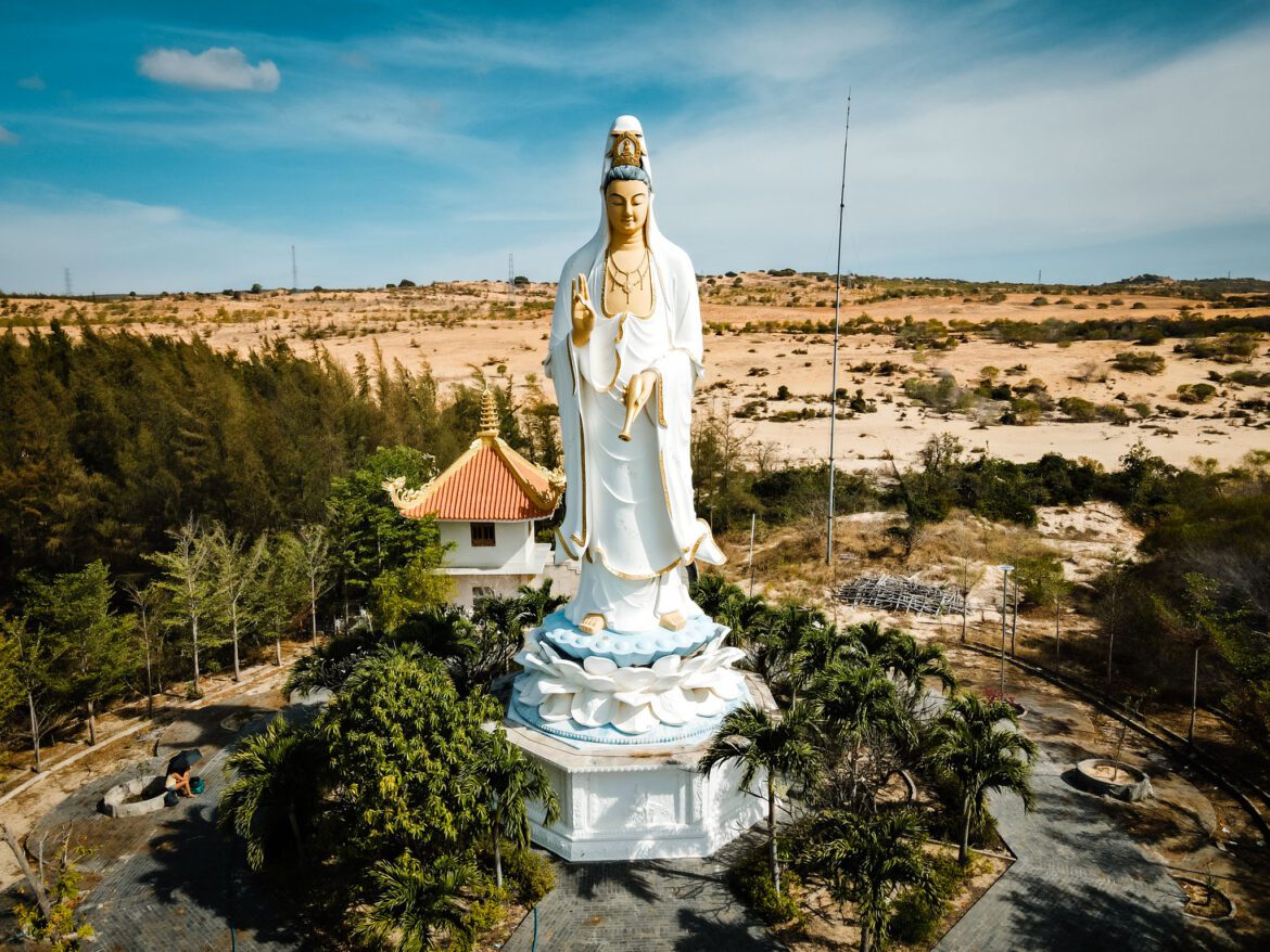 Large statue surrounded by scaffolding at a temple in Mui Ne, Vietnam under blue skies in the desert.