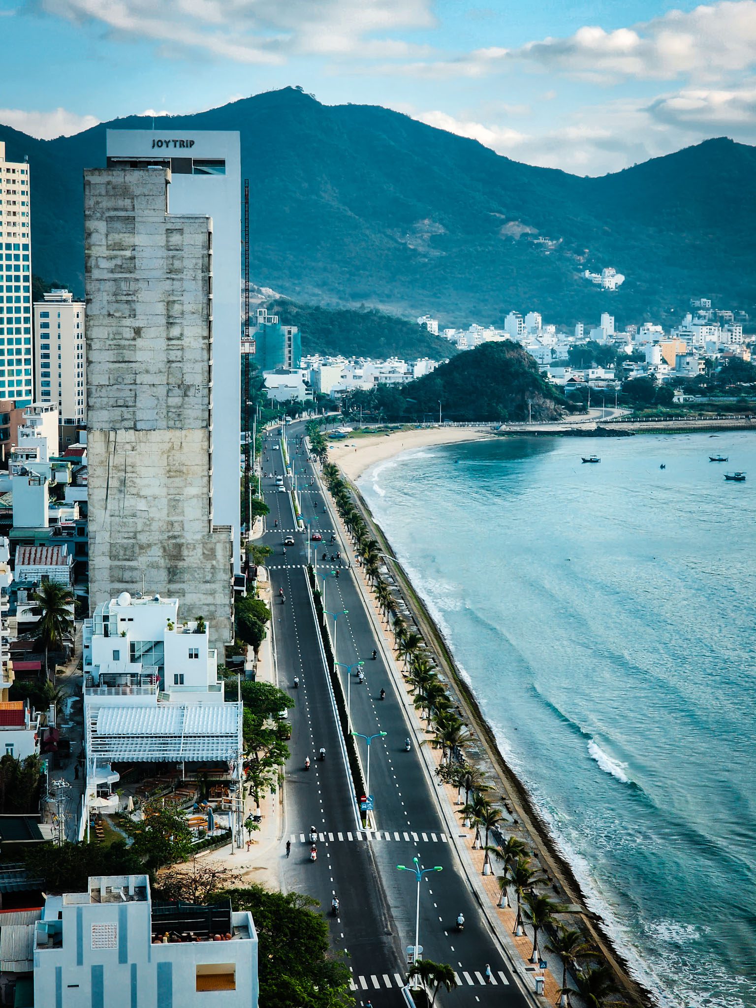 Coastal road and beach with mountains in the background, Nha Trang skyline visible.