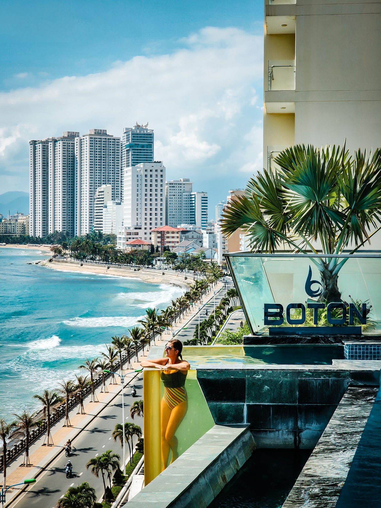 Woman relaxing in rooftop pool overlooking beach and city skyline in Nha Trang.