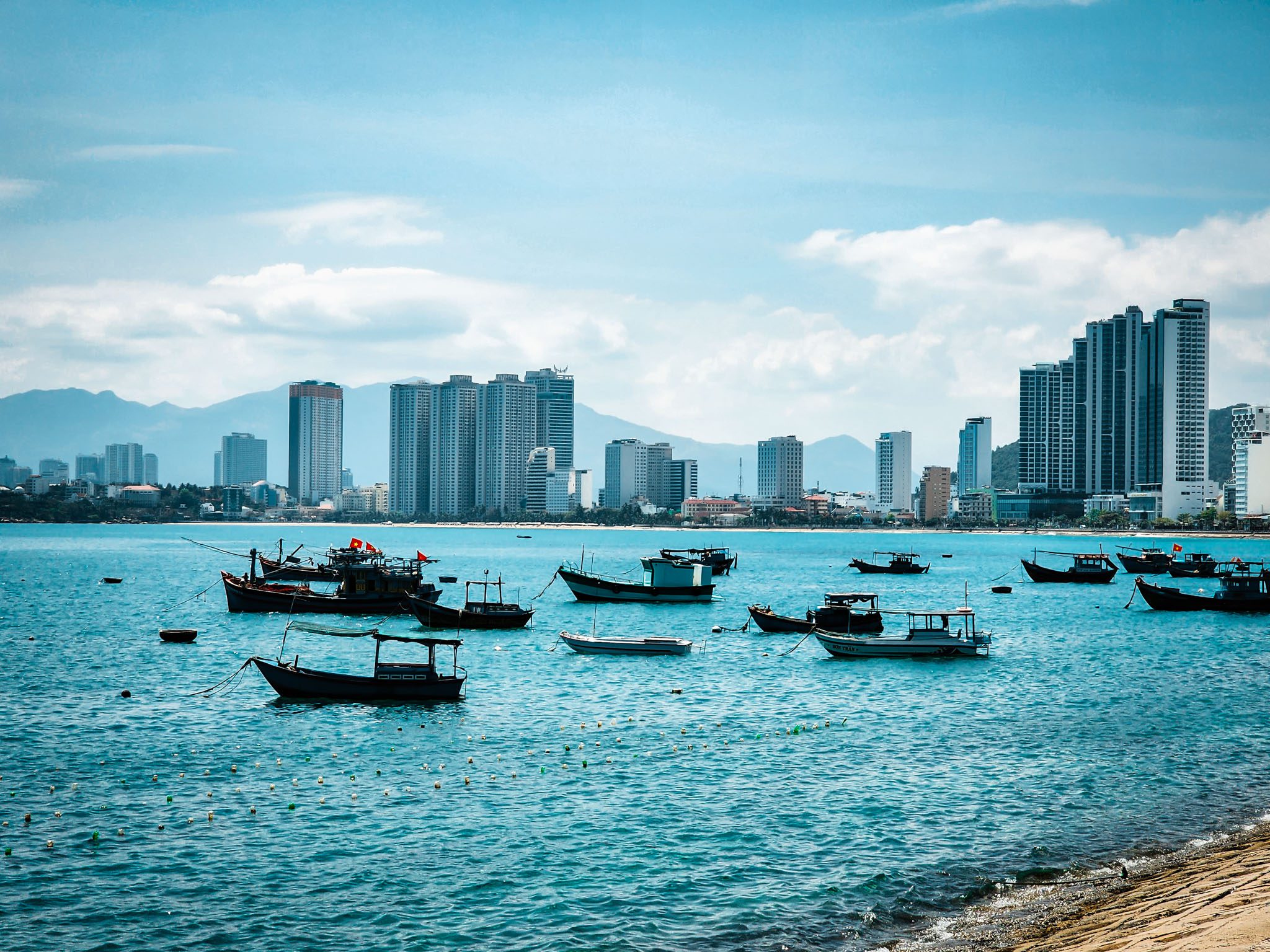 Boats float on the azure sea with Nha Trang's skyscrapers in the background.