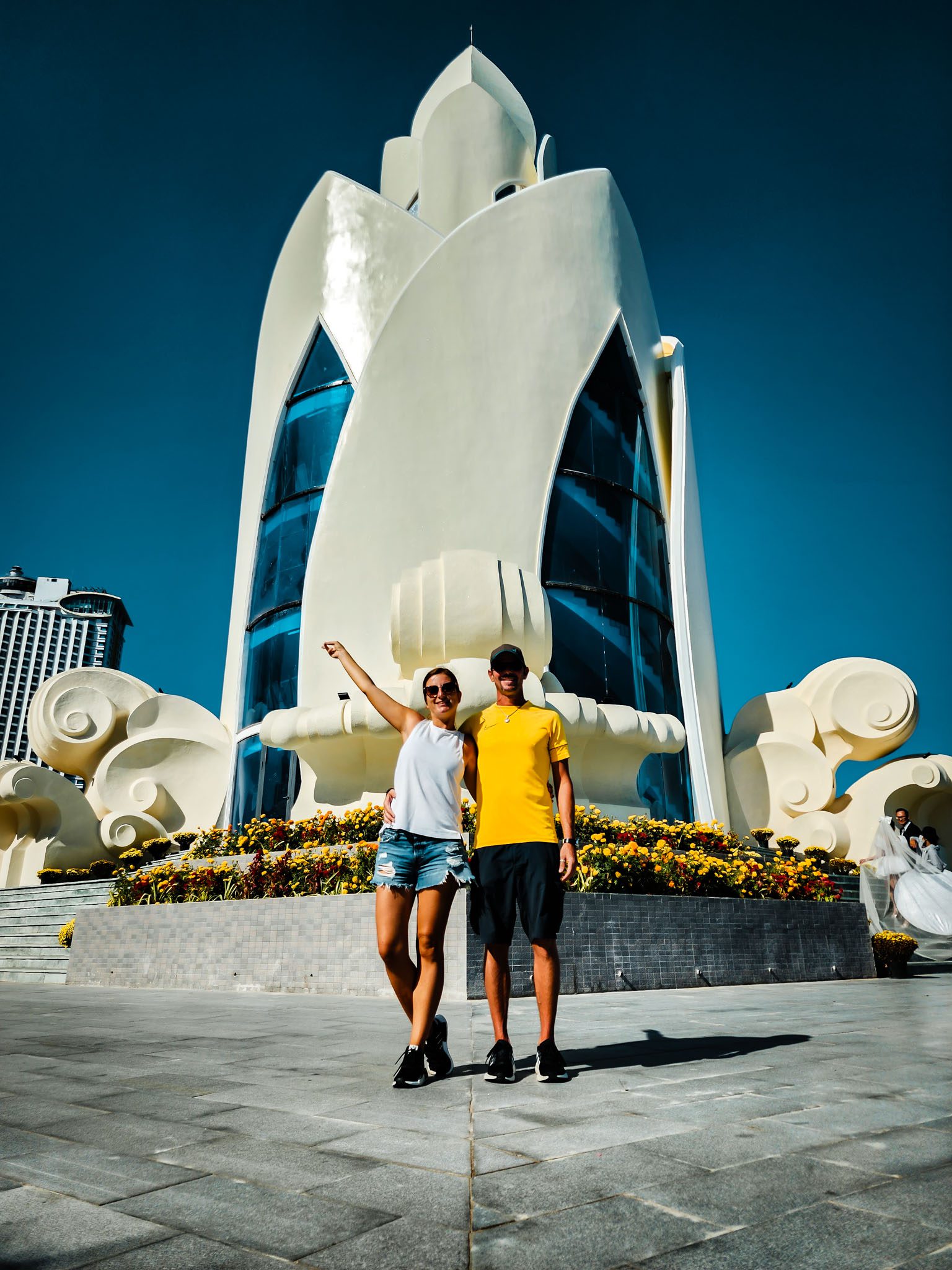 Couple posing in front of a modern white monument in Nha Trang under a clear blue sky.