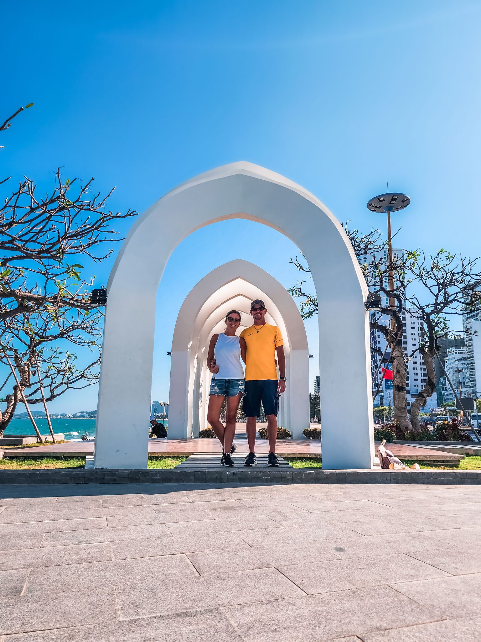 Couple posing under a white arch by the sea in Nha Trang.
