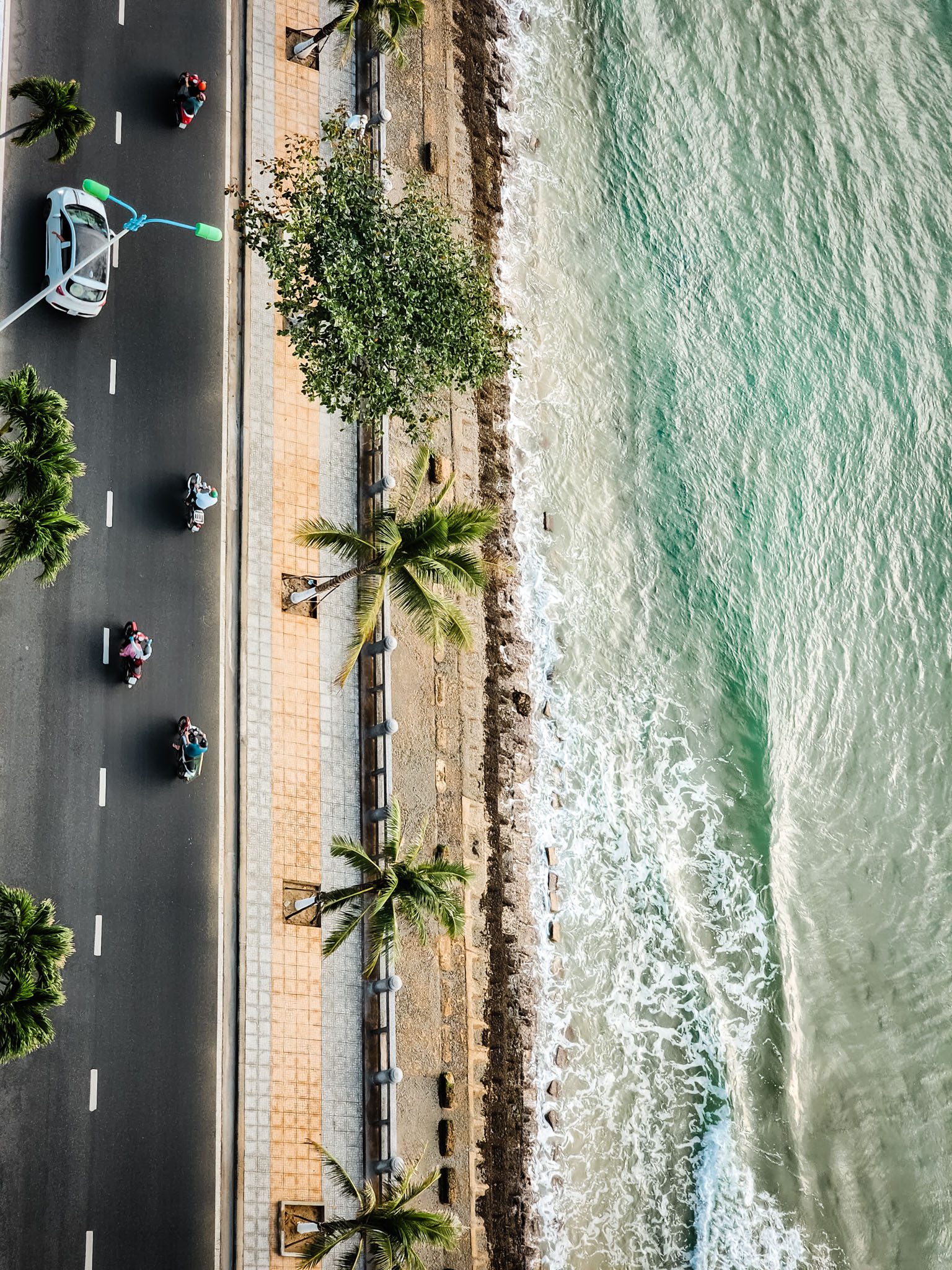 Aerial view of Nha Trang beachfront road with motorbikes, palm trees, and turquoise waves.