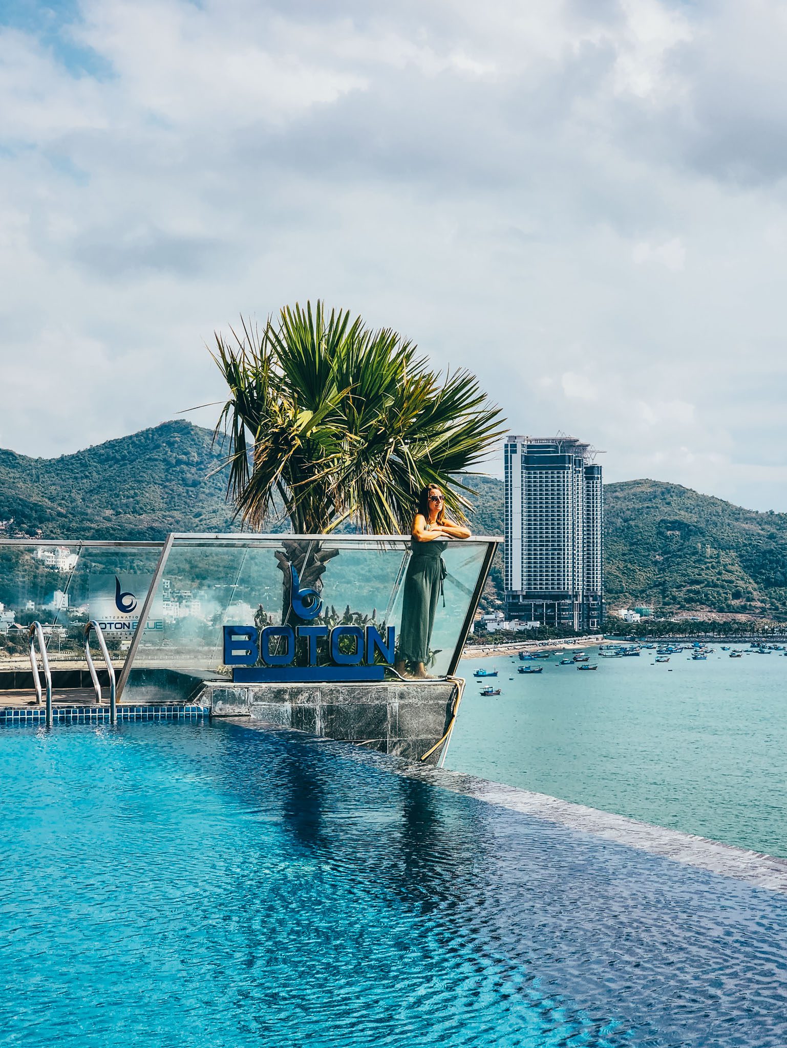Infinity pool with ocean view in Nha Trang, overlooking mountains and boats.